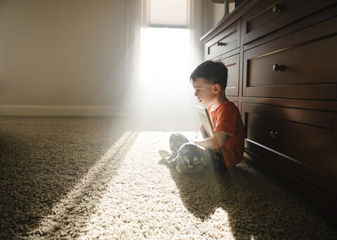 Side view of thoughtful boy with book sitting on rug at home stock photo