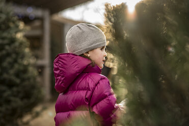 Seitenansicht eines Mädchens, das eine Kapuzenjacke trägt, während es bei den Weihnachtsbäumen im Hof steht - CAVF54888