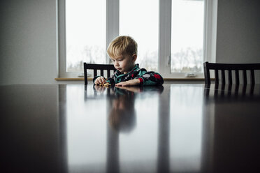 Junge spielt mit Spielzeug auf dem Tisch, während er zu Hause sitzt - CAVF54895