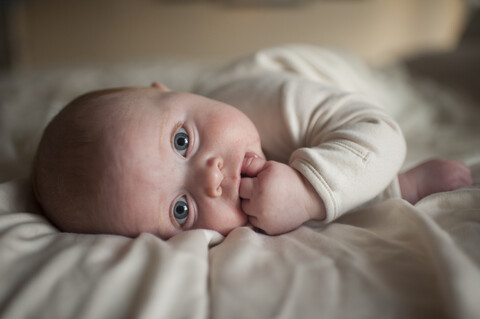 Porträt eines süßen kleinen Jungen mit Finger im Mund auf dem Bett liegend, lizenzfreies Stockfoto