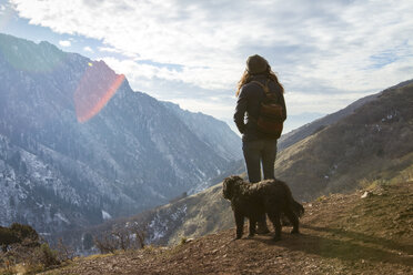 Frau mit Hund, die im Winter auf einem Berg stehend die Aussicht genießt - CAVF54926