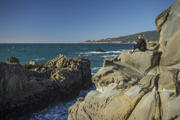 Seitenansicht einer Frau, die auf einem Felsen am Strand sitzt, gegen einen klaren Himmel - CAVF54927