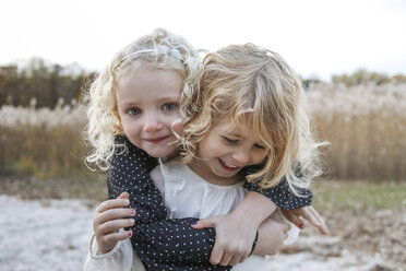 Portrait of girl embracing sister while standing against plants during winter - CAVF54948