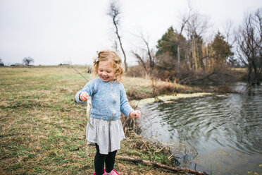 Cheerful girl holding fish while fishing by lake - CAVF54949