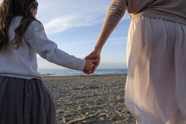 Mittelteil einer Mutter, die ihre Tochter an der Hand hält, während sie am Strand gegen den Himmel bei Sonnenuntergang spazieren geht - CAVF54951