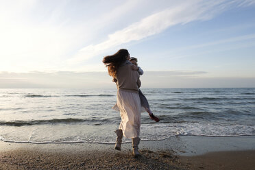 Rückansicht einer glücklichen Mutter, die ihre Tochter am Strand gegen den Himmel bei Sonnenuntergang dreht - CAVF54953