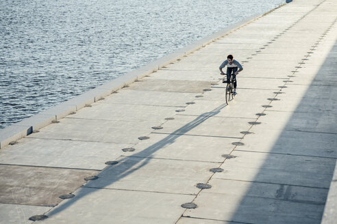 Junger Mann fährt Fahrrad auf der Uferpromenade am Flussufer - VPIF01036