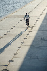 Junger Mann fährt Fahrrad auf der Uferpromenade am Flussufer - VPIF01037