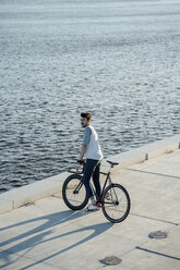 Junger Mann mit Fixie-Fahrrad macht eine Pause am Flussufer - VPIF01040