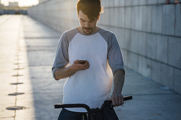 Junger Mann mit Pendler-Fixie-Fahrrad schaut auf sein Handy - VPIF01042