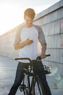 Lächelnder junger Mann mit Pendler-Fixie-Fahrrad schaut auf sein Handy - VPIF01043