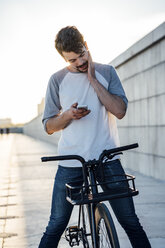 Junger Mann mit Pendler-Fixie-Fahrrad schaut auf sein Handy - VPIF01044