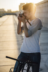 Young man with commuter fixie bike taking a picture at sunset - VPIF01046