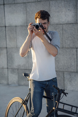 Junger Mann mit Pendler-Fixie-Fahrrad beim Fotografieren an einer Betonwand, lizenzfreies Stockfoto
