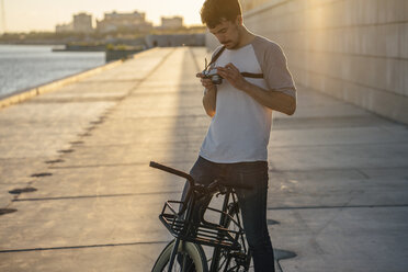 Junger Mann mit Fixie-Fahrrad und Kamera auf der Uferpromenade am Flussufer - VPIF01050