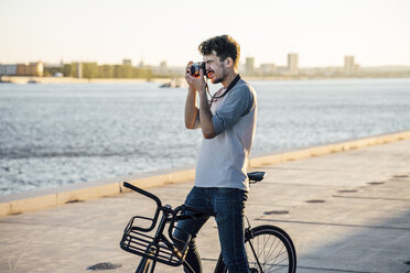 Junger Mann mit Pendler-Fixie-Fahrrad beim Fotografieren am Flussufer - VPIF01051