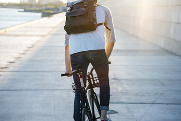 Rückansicht eines jungen Mannes mit Rucksack auf dem Fahrrad auf der Uferpromenade bei Sonnenuntergang - VPIF01056