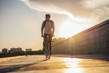 Junger Mann mit Rucksack fährt Fahrrad auf der Promenade bei Sonnenuntergang - VPIF01061