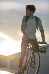 Junger Mann mit Rucksack fährt Fahrrad auf der Promenade bei Sonnenuntergang - VPIF01062