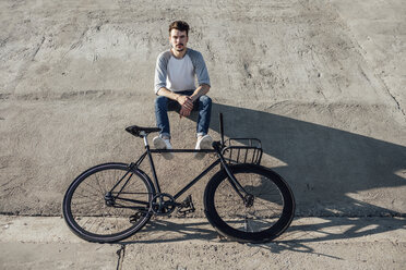 Junger Mann mit Pendler-Fixie-Fahrrad macht eine Pause auf einer Betonwand sitzend - VPIF01069