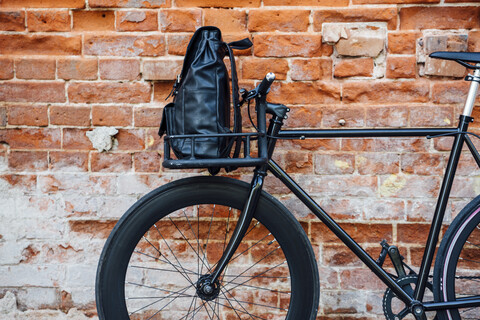 Rucksack in der Gepäckablage eines umgebauten Fixie-Fahrrads an einer Mauer, lizenzfreies Stockfoto