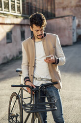 Young man with commuter fixie bike on a backyard in the city checking cell phone - VPIF01095