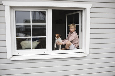 Porträt eines auf der Fensterbank sitzenden Jungen mit Jack Russel Terrier und Siamkatze, der aus dem offenen Fenster schaut - KMKF00645