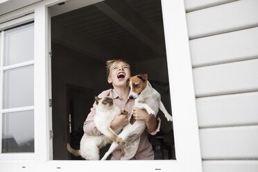 Junge steht mit Jack Russel Terrier und Siamkatze am offenen Fenster - KMKF00646