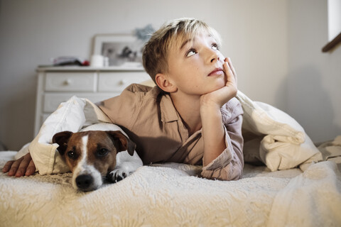 Porträt eines blonden Jungen und seines Jack Russel Terriers, die zusammen auf einem Bett liegen, lizenzfreies Stockfoto
