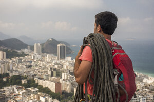 Kletterer mit Kletterseil auf der Schulter mit Blick auf die Landschaft über Copacabana, Rio de Janeiro, Brasilien - AURF07712