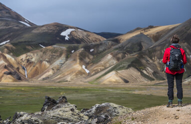 Hiker admiring rhyolite mountains at Landmannalaugar on Laugarvegur hiking trail, Landmannalaugar, Fjallabak, Iceland - AURF07727