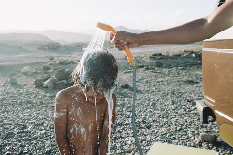 Junge duscht im Freien am Kopfsteinpflasterstrand, Teneriffa, Kanarische Inseln, Spanien, lizenzfreies Stockfoto