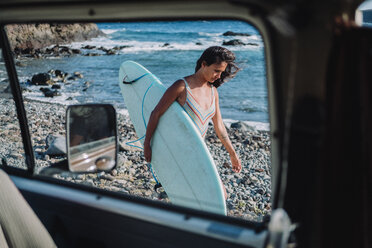 Blick aus dem Innenraum eines Autos auf eine Frau, die mit ihrem Surfbrett am Strand spazieren geht, Teneriffa, Kanarische Inseln, Spanien - AURF07780