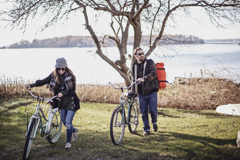 Couple walking bikes across grassy lawn, Peaks Island, Maine, USA - AURF07809