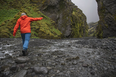 Mann balanciert über Felsen, um den Fluss in der Stakholtsgja-Schlucht im Thorsmork-Tal zu überqueren, Thorsmork, Sudurland, Island - AURF07867