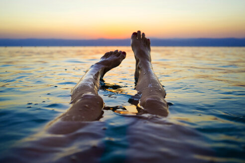 Füße einer im Toten Meer schwimmenden Frau bei Sonnenuntergang, Madaba Governorate, Jordanien - AURF07876