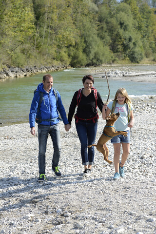 Familie beim Wandern mit Rucksack und Hund an der Isar, Oberbayern, Deutschland, lizenzfreies Stockfoto