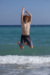 Portrait of redheaded young man jumping in the air at seashore - LBF02232