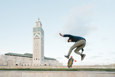 Seitenansicht eines Mannes, der mit dem Skateboard gegen die Moschee Hassan II fährt, lizenzfreies Stockfoto