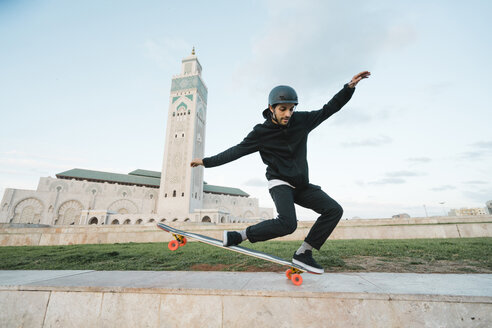 Mann führt Stunt auf Skateboard vor der Moschee Hassan II in voller Länge aus - CAVF54974