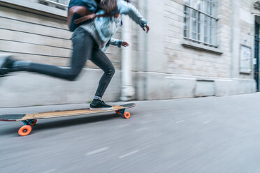 Unscharfe Bewegung einer Frau, die auf dem Fußweg bei einem Gebäude in der Stadt Skateboard fährt - CAVF54977