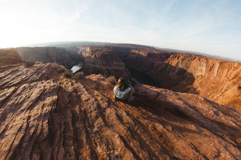 Rückansicht einer Frau, die auf einer Felsformation am Horseshoe Bend sitzt, gegen den Himmel, lizenzfreies Stockfoto