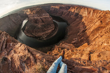 Low section of woman sitting on rock formation at Horseshoe Bend against sky - CAVF54979