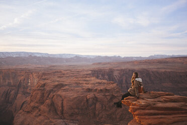Full length of woman sitting on rock formation at Horseshoe bend against sky - CAVF54980