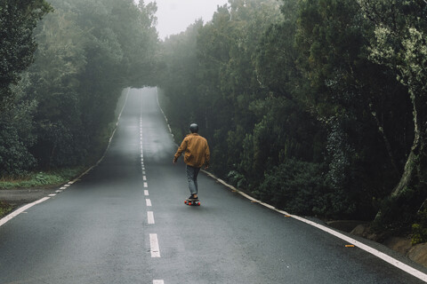 Rear view of man skateboarding on road amidst forest at Garajonay National Park stock photo