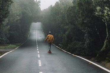 Rear view of man skateboarding on road amidst forest at Garajonay National Park - CAVF54986