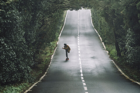 Mann fährt Skateboard auf der Straße inmitten des Waldes im Garajonay-Nationalpark, lizenzfreies Stockfoto