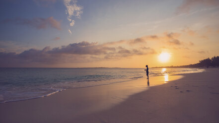 Side view of silhouette boy standing on shore at beach against sky during sunset - CAVF54992