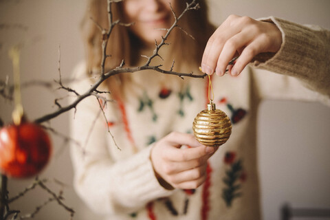 Mittelteil einer Frau, die zu Weihnachten zu Hause eine Weihnachtskugel an einen Zweig hängt, lizenzfreies Stockfoto