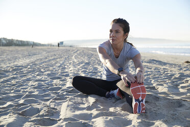 Confident woman stretching leg while exercising at beach - CAVF55014